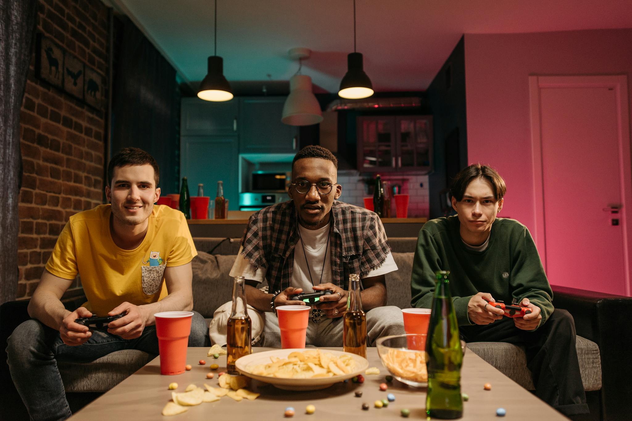 Three young men playing video games in a cozy living room with snacks and drinks.